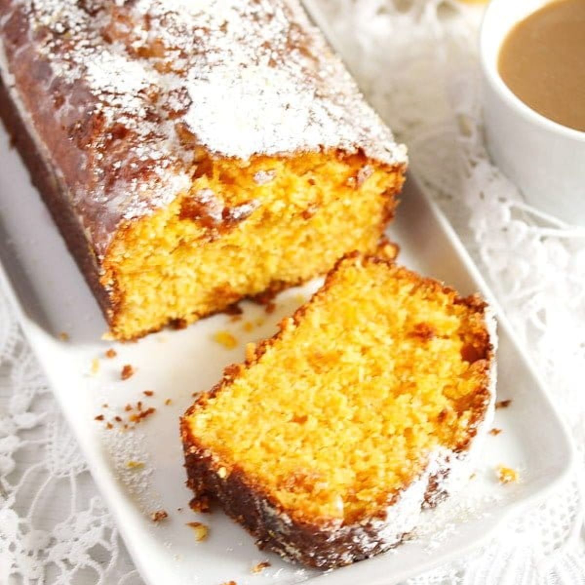 sliced carrot and coconut cake sprinkled with powdered sugar and a cup of tea.
