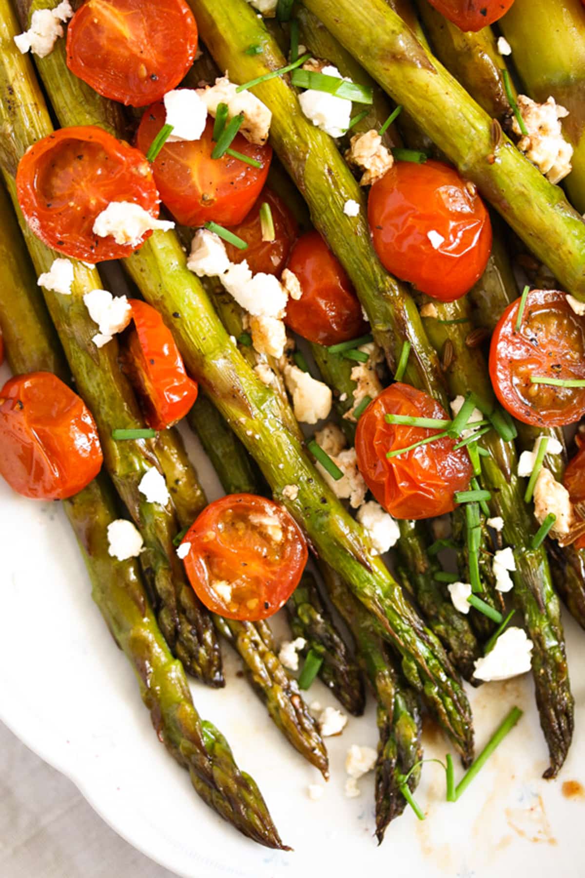 roasted cherry tomatoes and asparagus with feta on a platter.