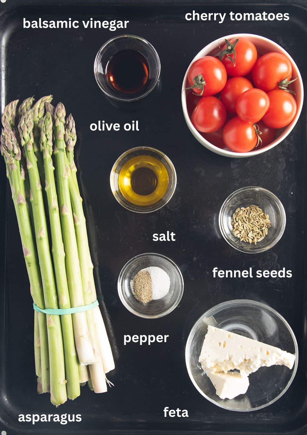labeled ingredients for roasting asparagus with cherry tomatoes, oil, fennel seeds, balsamic and feta.