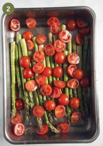 asparagus and halved cherry tomatoes in a roasting pan before baking.