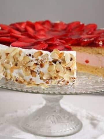 strawberry yogurt cheesecake with fresh strawberry topping on a tall cake platter.