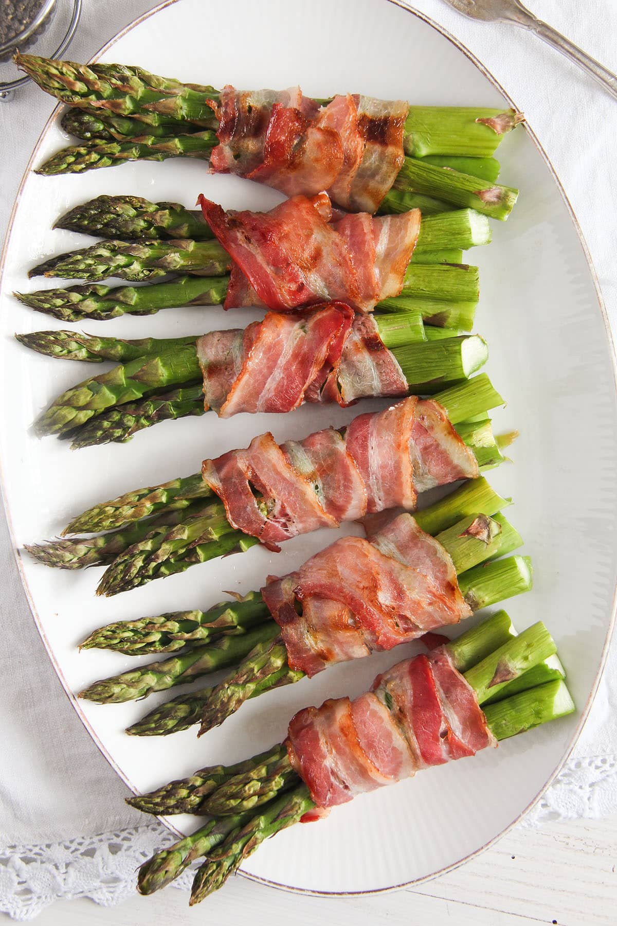 six asparagus and bacon bundles on an oval plate.