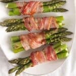 four bacon-wrapped asparagus bundles on a platter.