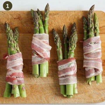 four bundles of asparagus wrapped in bacon on a wooden board before cooking.