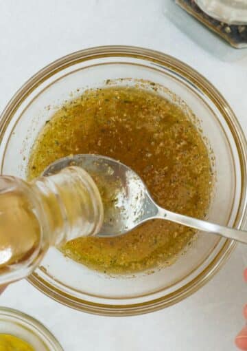 adding one tablespoon of olive oil to a bowl of salad dressing.