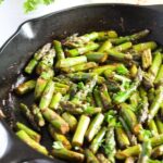 sauteed asparagus with garlic, parsley and soy sauce in a cast iron pan.