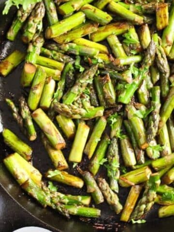 close up of sauteed asparagus with garlic in a cast iron skillet.