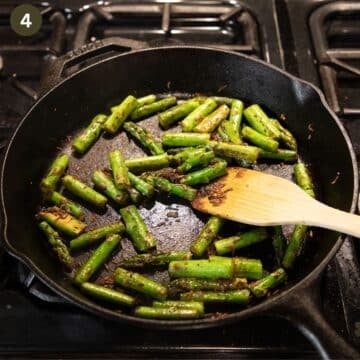 stirring asparagus pieces with a wooden spatula in a cast iron skillet.