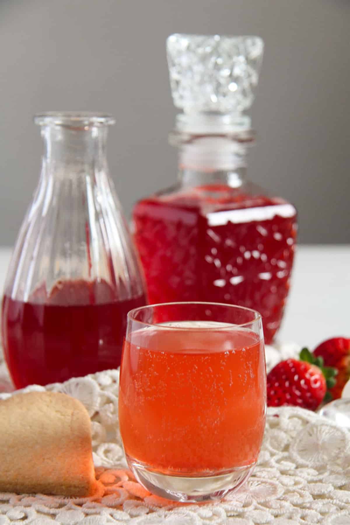 strawberry syrup in two cute bottles and one glass of prepared syrup.