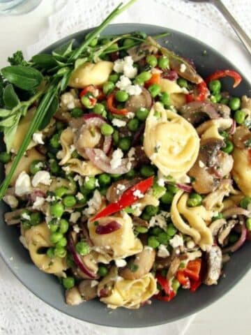 summer tortellini salad with mushrooms, peas and herbs in a grey bowl.