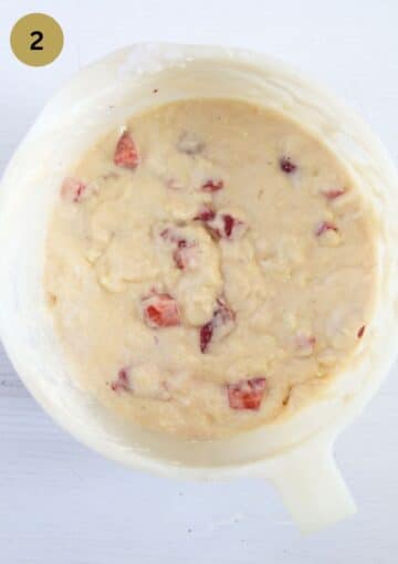 muffin batter with strawberry pieces inside in a mixing bowl.