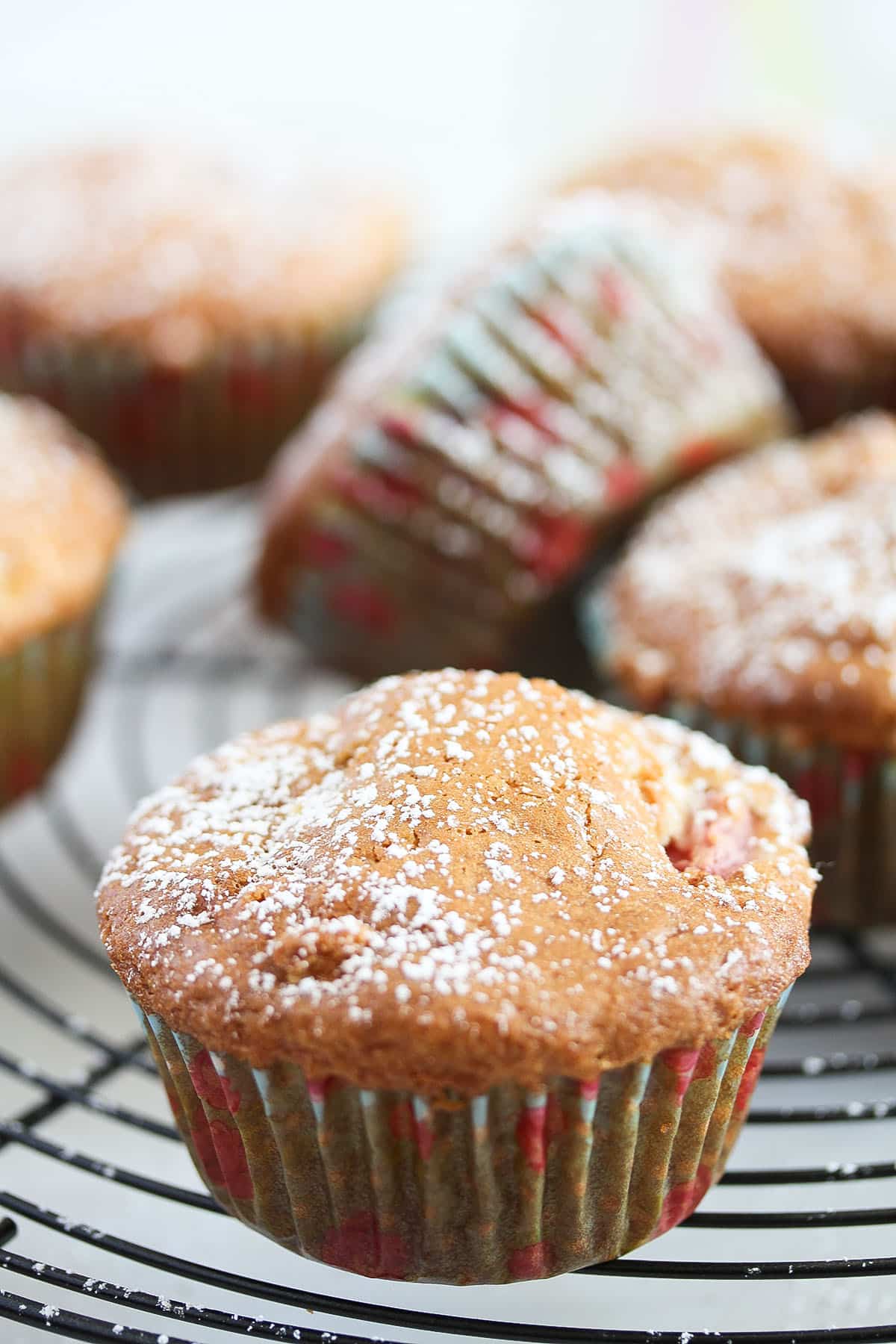 strawberry and white chocolate muffins sprinkled with icing sugar on a rack.