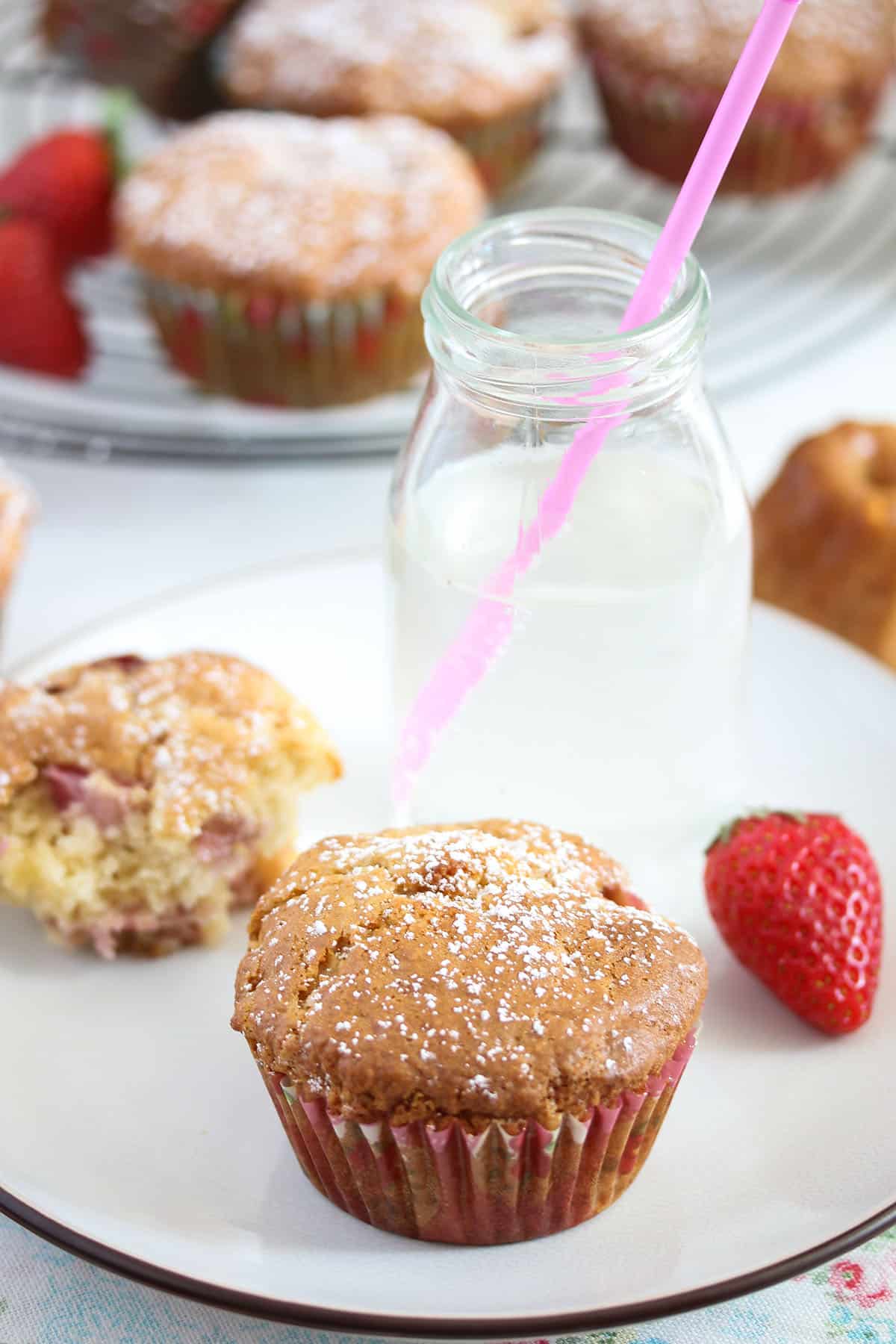 strawberry muffins, fresh strawberries and a small bottle of mik with a pink straw in it.