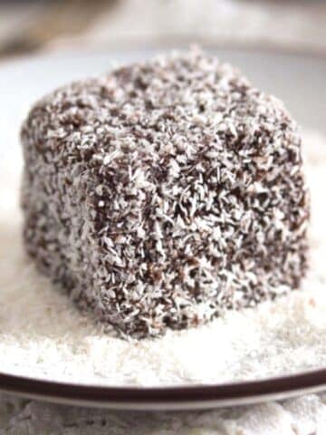 lamington cake close up on a white plate with coconut flakes around it