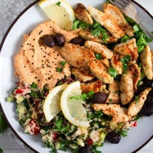 chicken shawarma plate with hummus, tabbouleh, olives and lemon wedges.