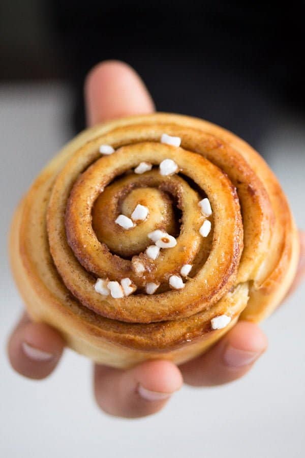 a hand holding a Swedish kanelbullar cinnamon bun