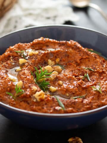 syrian muhammara dip topped with herbs in a small blue bowl.