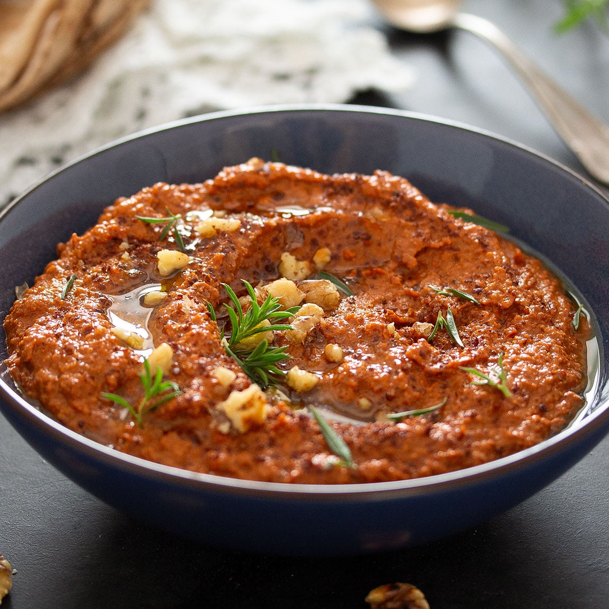 syrian muhammara dip topped with herbs in a small blue bowl.