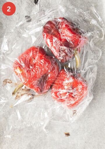 three roasted red peppers covered with plastic wrap.