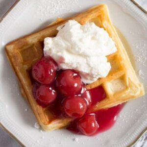 german waffle topped with cherries and cream on a vintage plate.