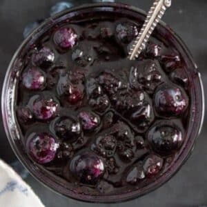 large and glossy canned blueberry sauce in a jar with a spoon in it.