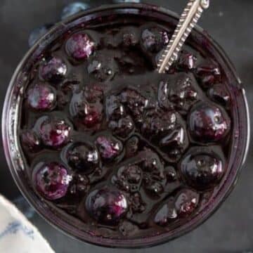large and glossy canned blueberry sauce in a jar with a spoon in it.