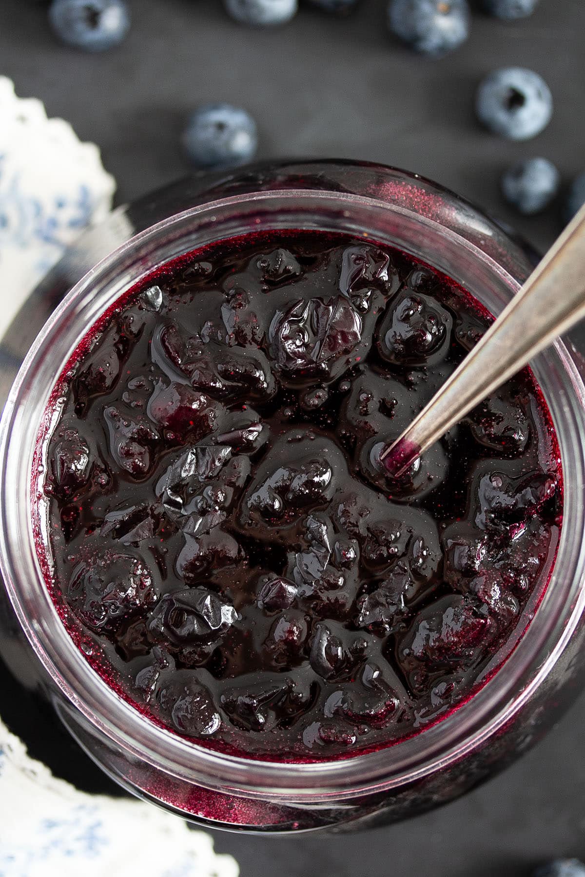 blueberry sauce in a jar with fresh berries around it.