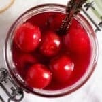 overhead view of a small jar of cherry sauce with a spoon in it.