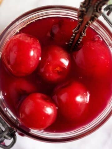 overhead view of a small jar of cherry sauce with a spoon in it.
