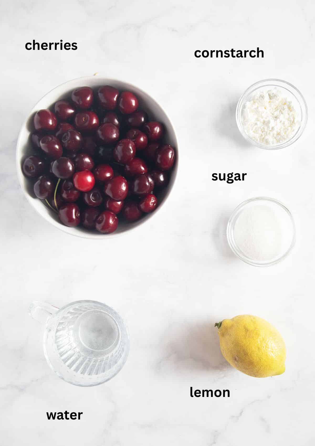 flat lay of labeled ingredients for making cherry sauce with sweet cherries, cornstarch, lemon, water, and sugar.
