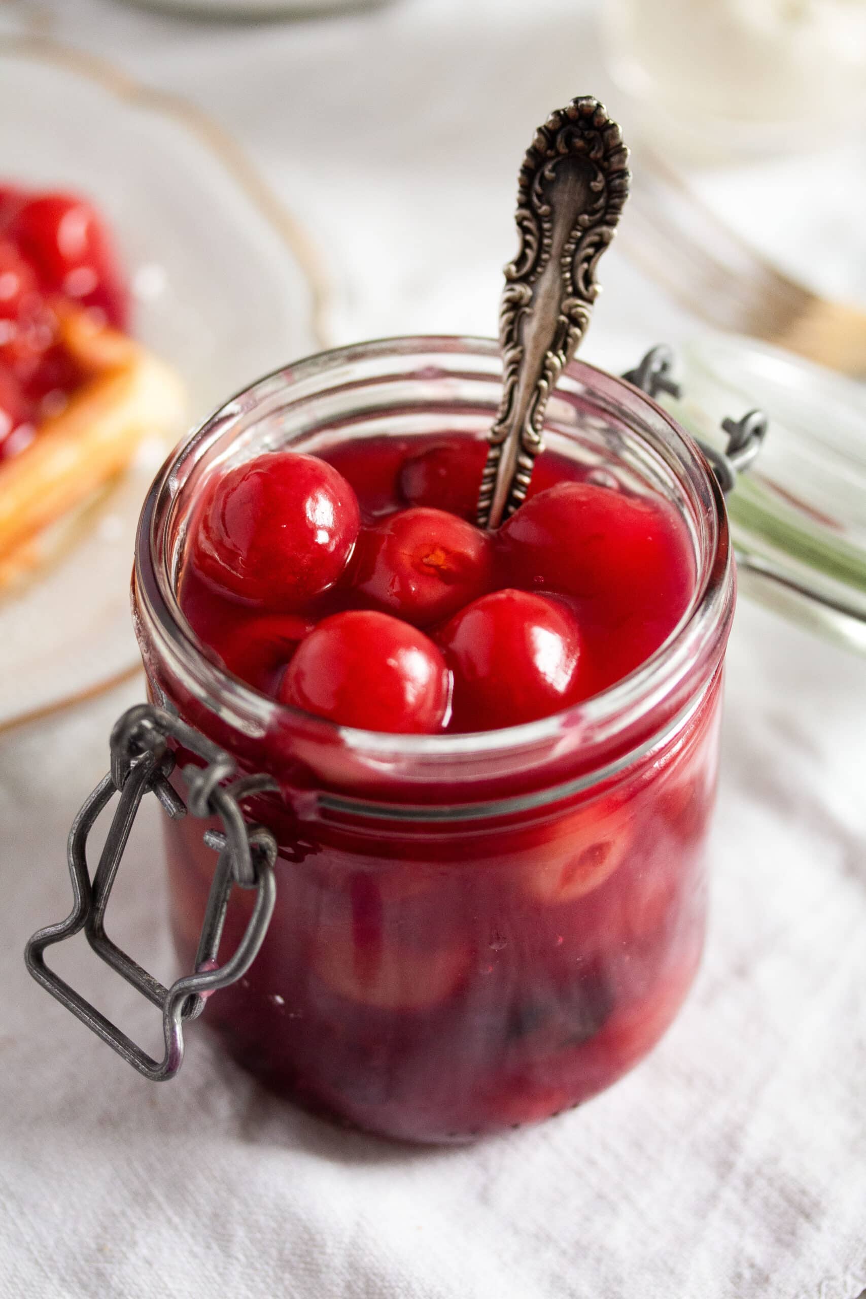 jar with cherries in sauce with a spoon in it.
