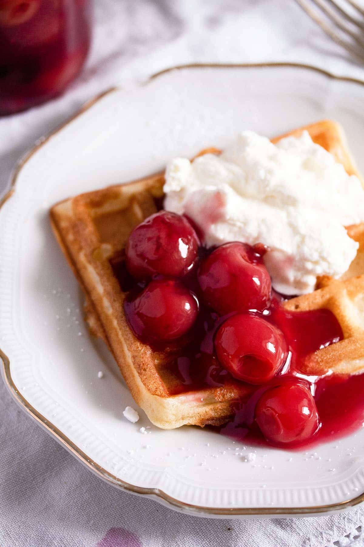 waffel served with cherry sauce and whipped cream on a small plate.