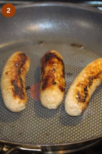 three sausages cooking in a pan.