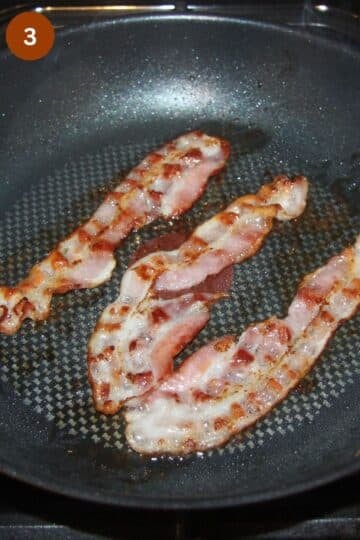 three rashers of bacon cooking in a pan.