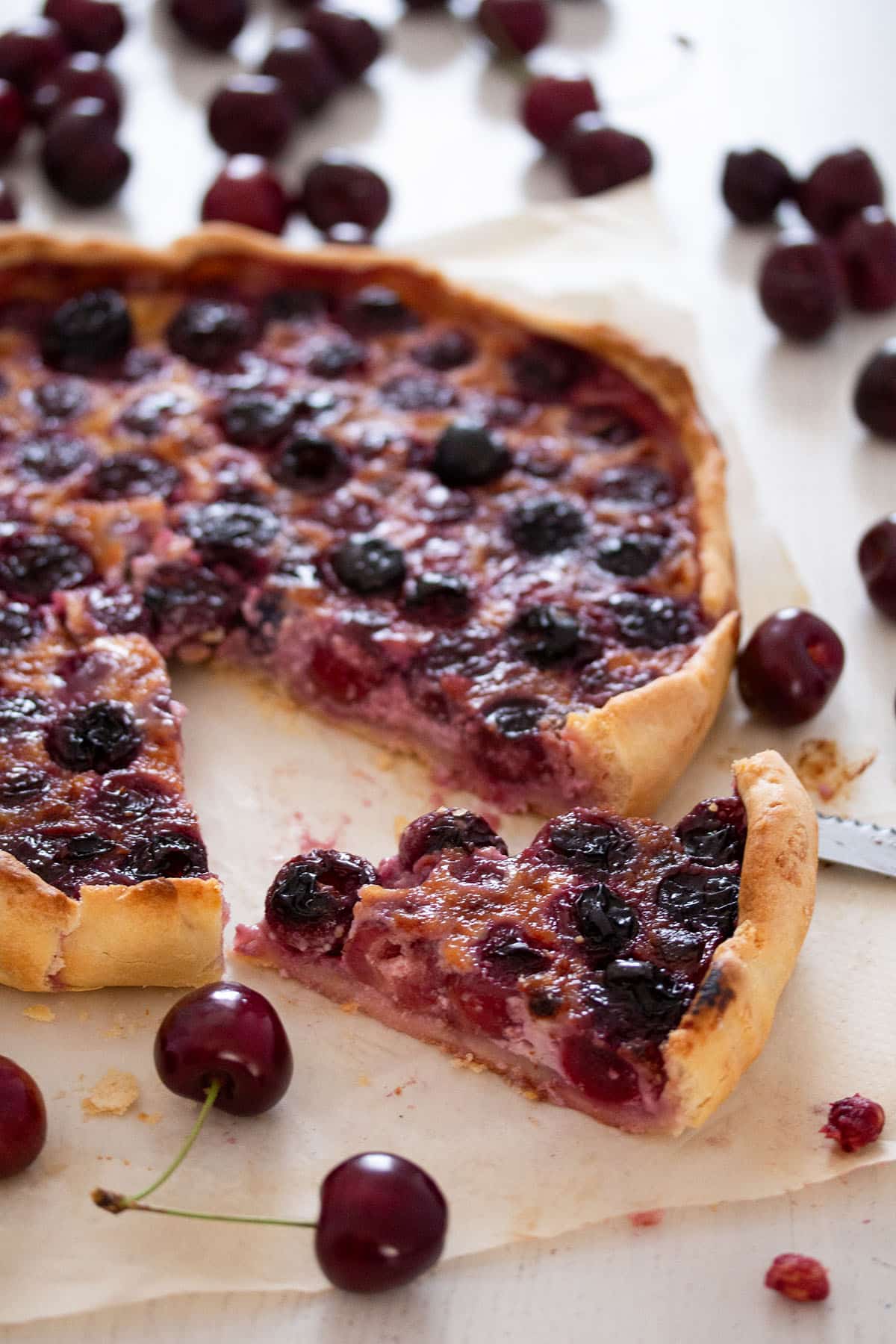swiss cherry pie with one sliced piece in front and many fresh cherries around it.