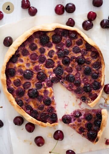 swiss kirschwähe with a cut slice on a cake lifter and fresh cherries around it.