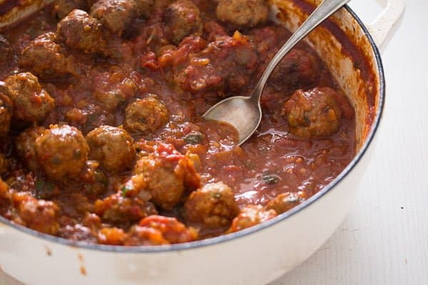 stirring meatballs in the sauce in a large pan with a spoon