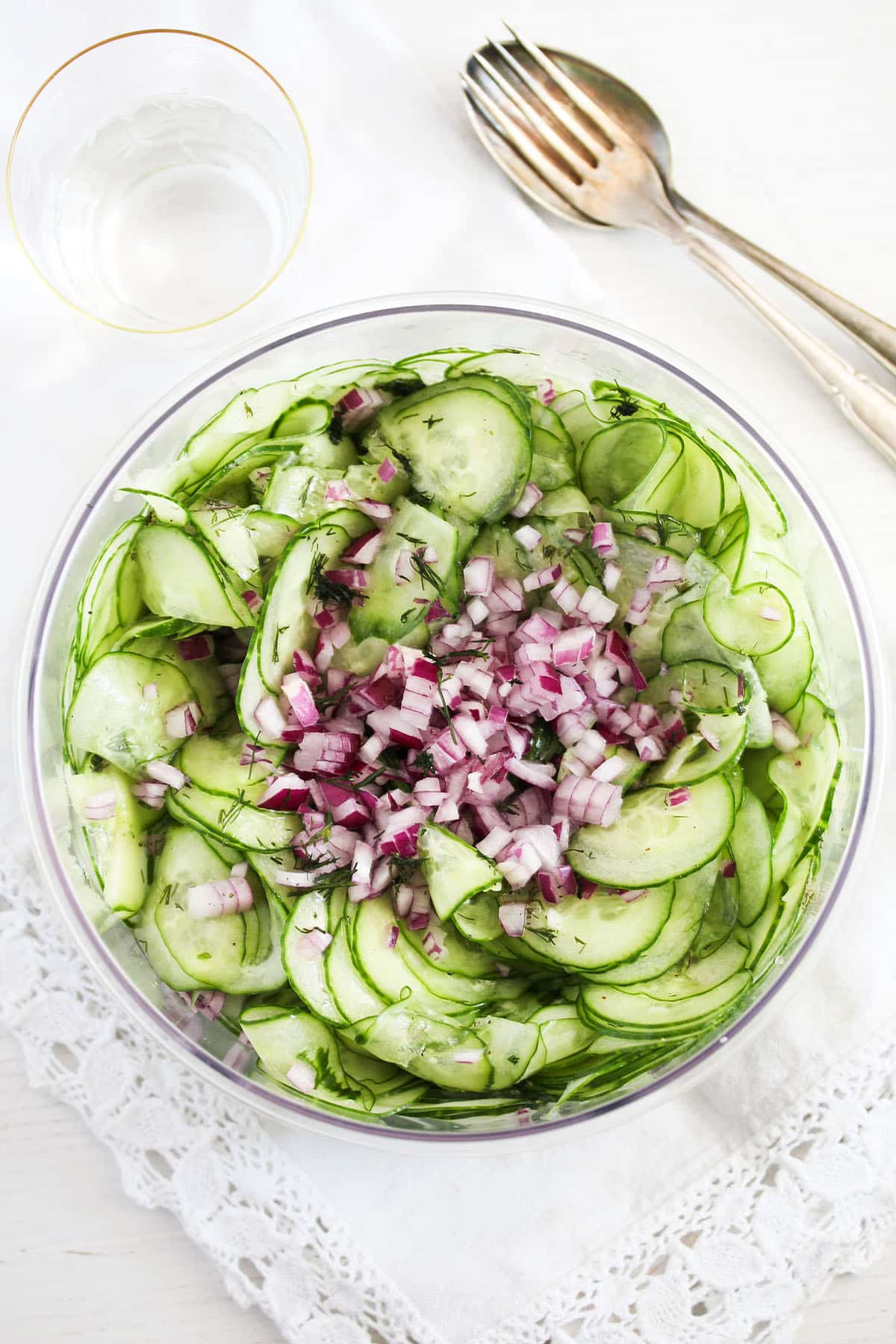 cucumber salad with red onions and vinaigrette in a bowl, a fork and spoon on the side.