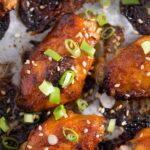 close up red chicken wings sprinkled with sesame and green onions