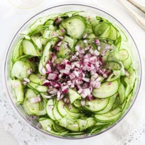 oil and vinegar cucumber salad with chopped red onions on top.