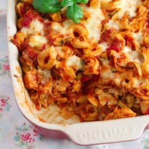 baked tortellini with tomatoes and mozzarella and basil in a baking dish.