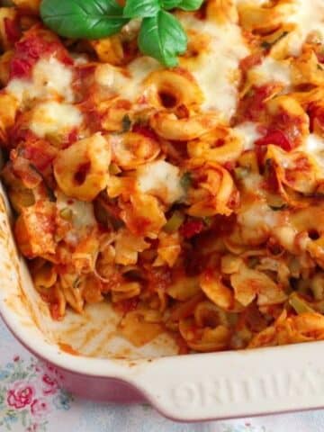baked tortellini with tomatoes and mozzarella and basil in a baking dish.