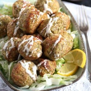 many broccoli and cauliflower balls sprinkled with mayo and served with lettuce and lemon wedges.