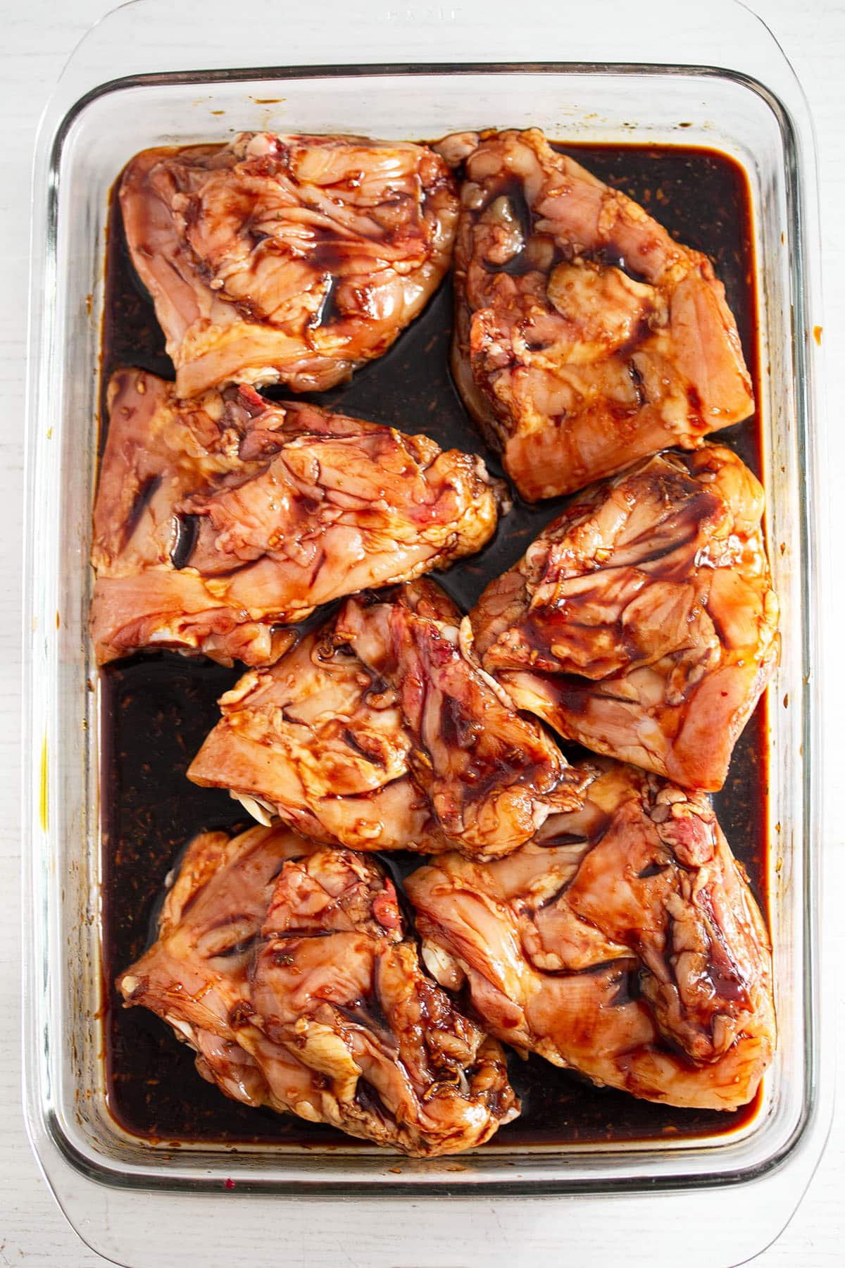 raw pieces of chicken marinating in honey lime marinade in a baking dish.