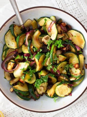 bowl with sauteed zucchini and onions with a spoon in it.