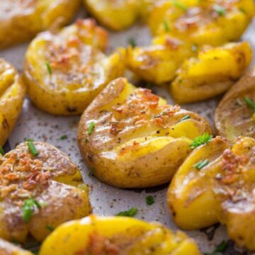 fingerling smashed potatoes sprinkled with chives on a baking sheet.