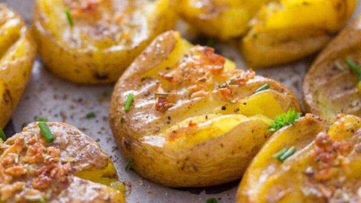 fingerling smashed potatoes sprinkled with chives on a baking sheet.
