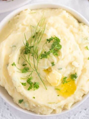 garlic parmesan mashed potatoes with herbs and melting butter on top.