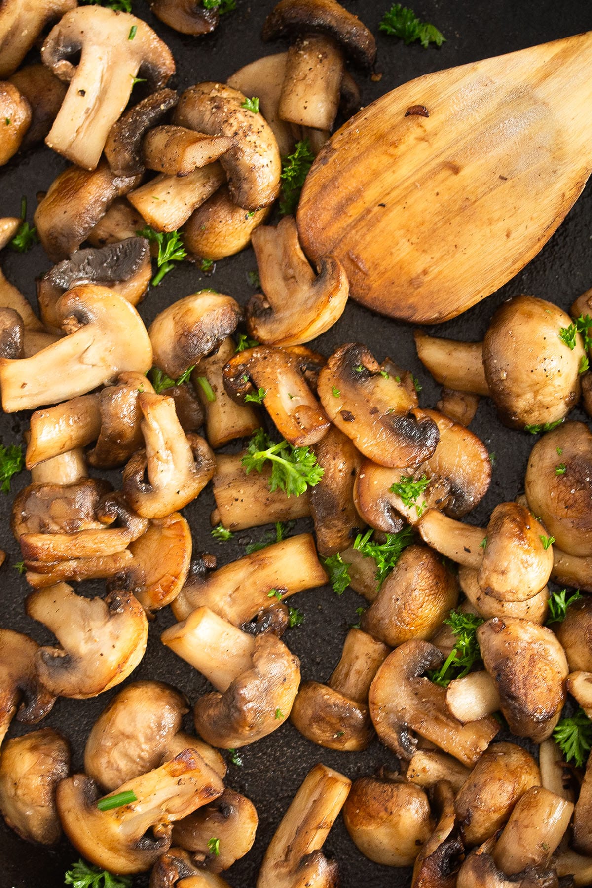 golden sauteed mushrooms for steak and a wooden spoon.