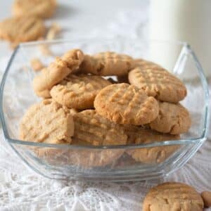peanut butter cookies with peanuts in a square glass bowl on a vintage table cloth.